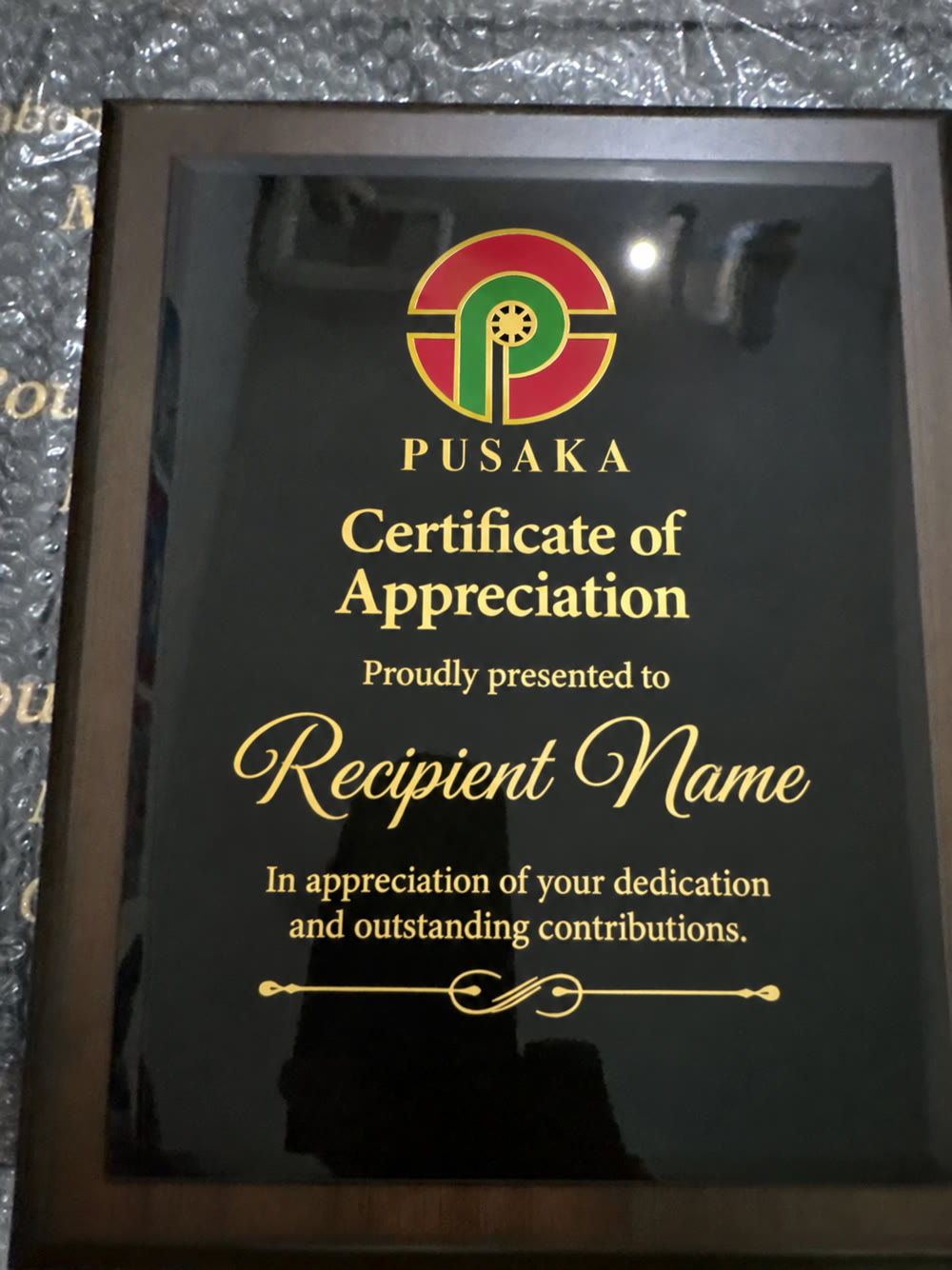Walnut plaque with black glass face, printed with the Pusaka logo in gold