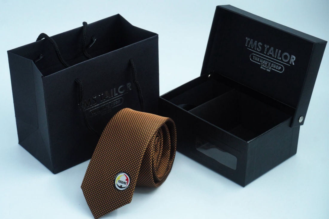 A brown TEGAS custom woven tie with a TMS Tailor box